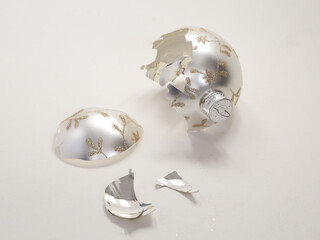 The shards and remnants of a classy broken Christmas bell ornament are shown in a closeup view, isolated against a white background.