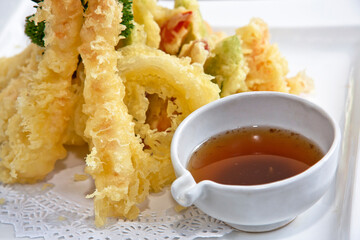 Shrimp and vegetable tempura with soy sauce, in a white square plate on wooden background, close up