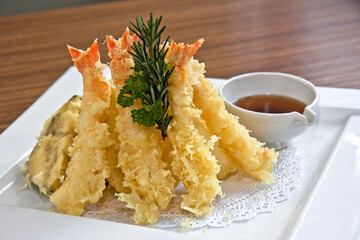 Shrimp and vegetable tempura with soy sauce, in a white square plate on wooden background, close up