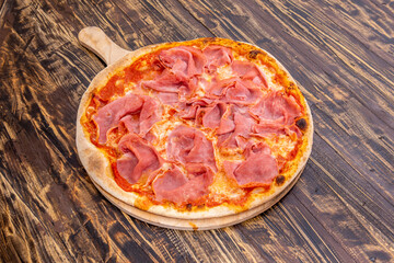 Pizza with prosciutto on dark wooden table