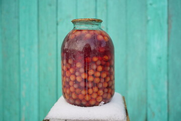 Close up of canned juice with berries on chair with snow on background of old green wooden house....