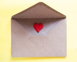 Love letter in a craft envelope with clay red heart on yellow background.