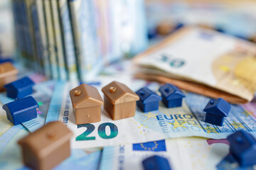House models on background of European twenty and fifty euro bills banknotes surrounded by coins.