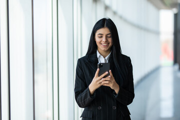 Businesswoman sending text messages using mobile phone. Young woman standing in her office