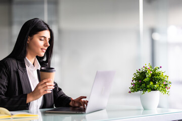 Attractive smiling business woman holding a cup of coffee sitting at office desk