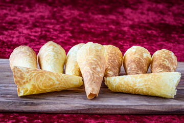 Norwegian Krumkake cookies on a rustic wood serving platter on a rich red background
