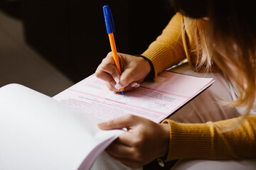 Latin woman hands writing and signing a document or a questionnaire in South America
