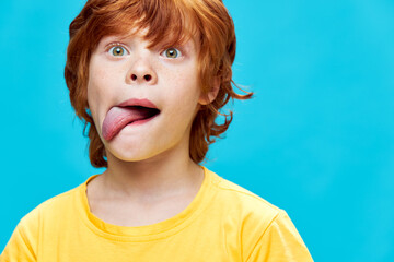 red-haired child pulls out his tongue to the side opens his eyes wide yellow t-shirt 