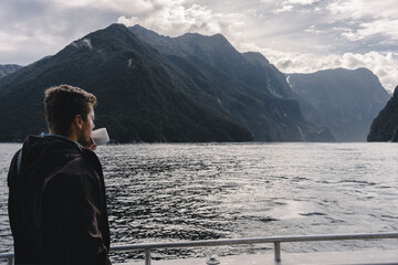 Naklejka premium Man drinking coffee on board of cruise in Milford Sound. Fiordland National Park, New Zealand