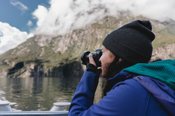 Young woman with camera taking pictures in Milford Sound. New Zealand travel destination
