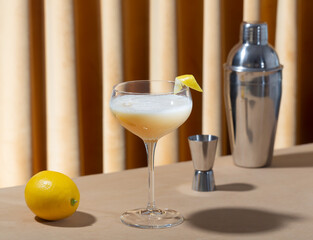 Glass filled with whiskey sour cocktail with lemon and shaker on the table