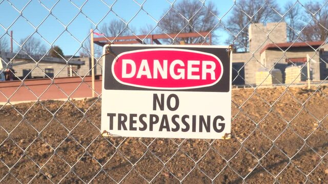 Bright red danger warning sign on temporary metal chain link fence built around urban building outdoor construction worker labor job site reading No Trespassing