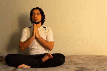 Young hispanic man with sportswear practicing yoga and meditation in his bed very calm and peaceful