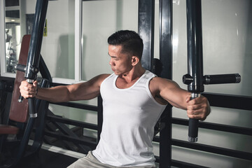 A muscular and fit asian man does some flys on the chest fly machine, also known as a pec deck at...
