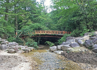 Fototapeta na wymiar Traditional vermilion orange bridge over rocky stream in Miyajima forest Japan