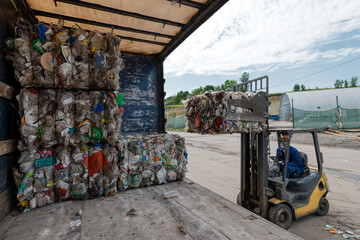 A forklift loads bales of compressed plastic bottles into a truck trailer. © nordroden