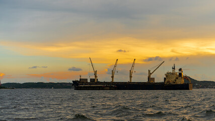 Fototapeta na wymiar Large cargo ship for logistic import export goods anchor at sea in evening with golden sunset