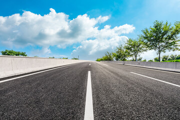 Fototapeta premium Asphalt road and green forest under blue sky.