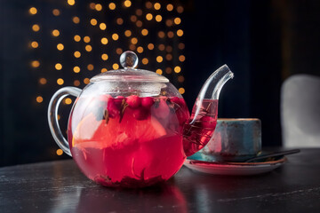 red tea with berries in a glass teapot and a blue cup on a wooden table