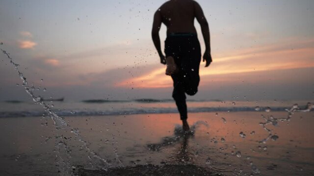 A young man splashes the water while sprinting or running  towards the sea during sunrise. Healthy lifestyle, Motivational or inspiration concept