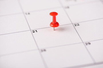 Close up view photo of red thumbtack on the 21 date on white calendar