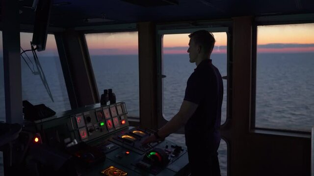 Navigation officer on ferry bridge looking through binoculars during sunset, medium shot