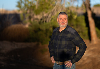 Portrait of an elderly man with a beard and gray hair. A photo with a very soft background in the evening at sunset in warm light. The senior is wearing jeans.