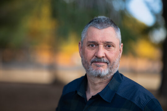 Portrait of an elderly man with a beard and gray hair. A close up with a very soft background in the evening at sunset in warm light. The senior looks friendly.