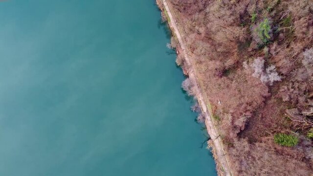 Straight down view drone footage of a trail around lake levico, in trentino, italy. The path is called "Strada dei pescatori", flying above the water
