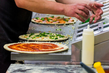 Cook in the kitchen putting the ingredients on the pizza. Production and delivery of food.