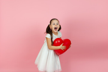 Obraz na płótnie Canvas Mock up a screaming, laughing girl in a white dress stands half-sideways and holds a red heart-shaped balloon isolated on a pink background.