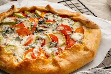 Close up homemade savory galette with vegetables, wheat pie with tomatoes, zucchini, blue cheese Gorgonzola. Rustic crust crostata on dark linen textile tablecloth.