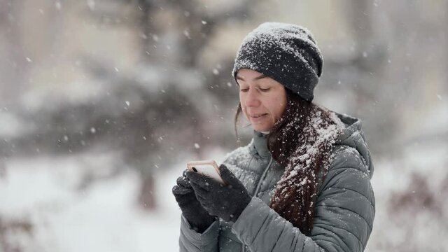 portrait of woman with smartphone outdoors at winter day, snowfall