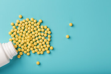 Yellow vitamins in the form of round dragees poured out of the jar on a blue background.