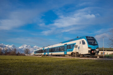 Modern diesel passenger train in white and blue color approaching small station of Rodica on a sunny winter day.
