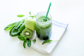 Healthy green smoothie with spinach in a mug with a strip of linen cloth on a white table background