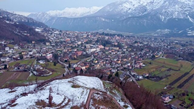 Drone footage aerial view of the levico terme town in trentino (Trento) city surrounded by mountains with snow from above