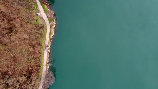 Straight down view drone footage of a trail around lake levico, in trentino, italy. The path is called "Strada dei pescatori", flying above the water