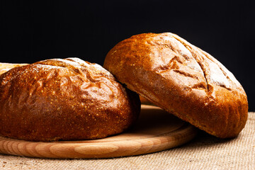 Two round rye breads on a cutting board. Dark colors, rustic style.