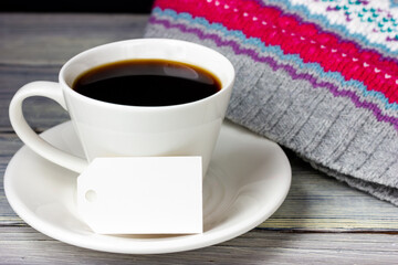 A cup of coffee and a white paper tag with place for text on a light wooden table.