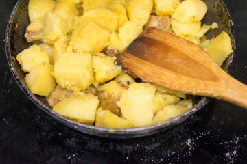Fried potatoes. Cast-iron pan. Wooden spatula. Homemade food.