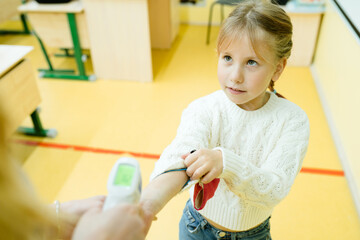 A little girl in a white sweater reached out her hand to have her temperature taken