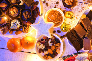 sweet food top view background for merry christmas or new year holiday decoration with night illumination - chocolate candies, tangerines, cookies on white wood