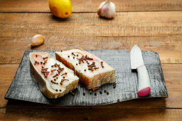 Cod fish steaks in fresh spices on a black wooden board next to a knife and garlic.