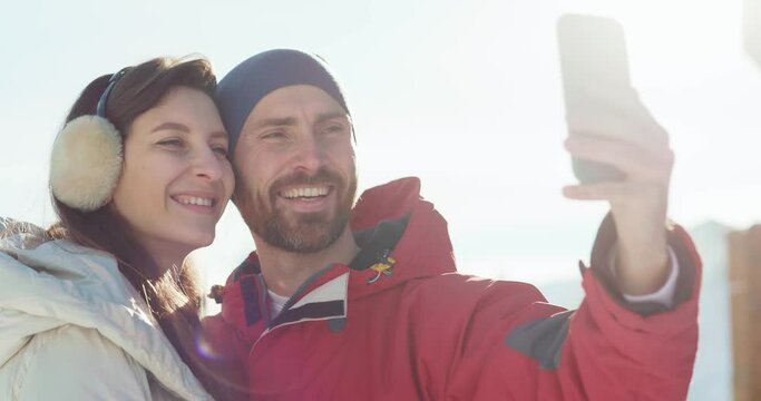 Adorable attractive caucasian couple taking family photo picture selfie on smartphone smiling against sunny sky. Winter season. Family and holidays. Technology.