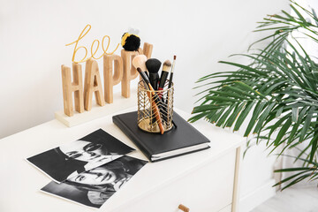 Chest of drawers with makeup  brushes and photos in interior of light room