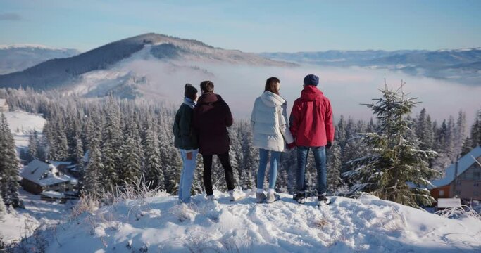 Four best friends company standing on mountain peak enjoying opening scenery. Winter holidays. Ski resort. Mountains. Friendship concept.