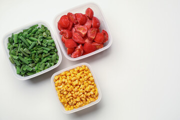 Plastic containers with different frozen vegetables on white background