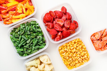 Plastic containers with different frozen vegetables on white background