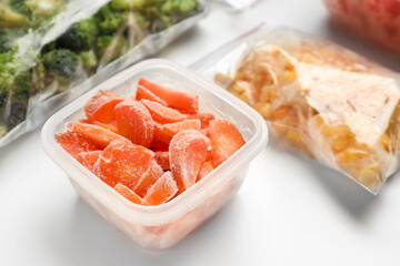 Container and plastic bags with frozen vegetables on white background